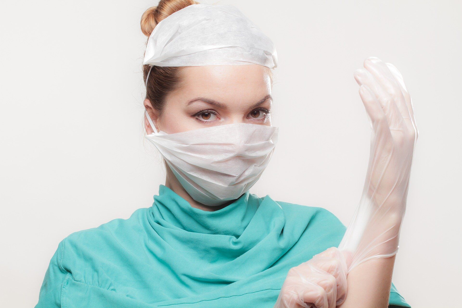 vinylhandschuhe-medizin Eine Krankenschwester im grünen Schutzkittel ziehst sich Vinyl Handschuhe an.