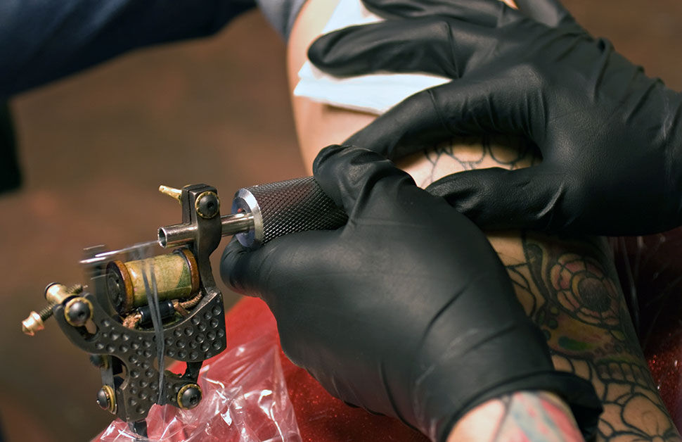 einweghandschuhe-tattoostudio Ein Tätowierer sticht einem Kunden ein neues Tattoo und trägt schwarze Vinyl Handschuhe.