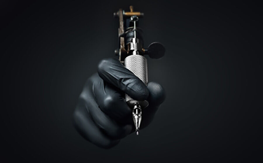 nitrilhandschuhe-tattoostudio Eine Person trägt schwarze Nitril Handschuhe und hält eine Tätowiermaschine in der Hand.