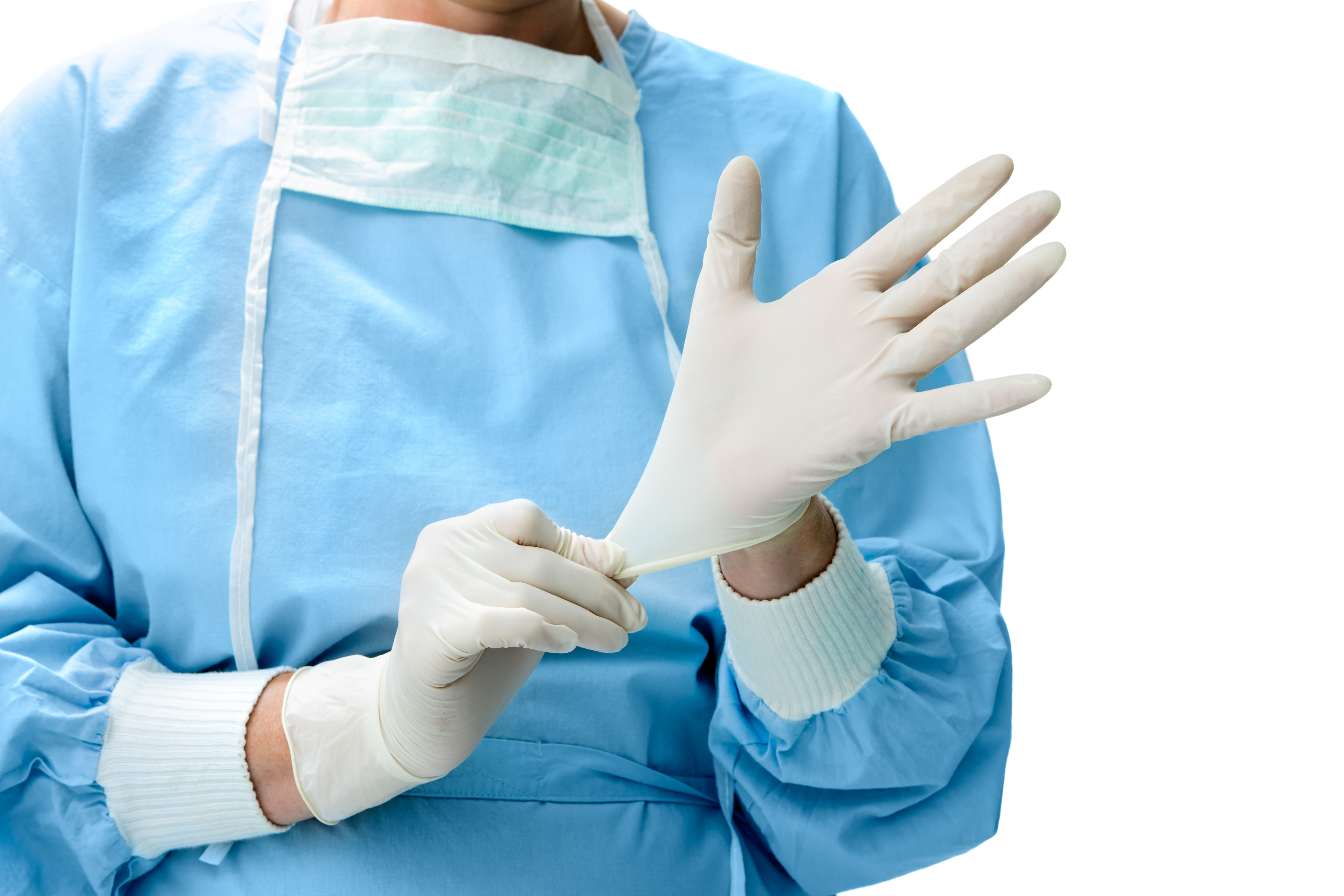 nitrilhandschuh-medizin Eine Ärztin trägt einen blauen Einwegkittel. Um ihren Hals hängt ein Mundschutz. Sie hat weiße Nitril Handschuhe an und zieht an dem einen Handschuh.